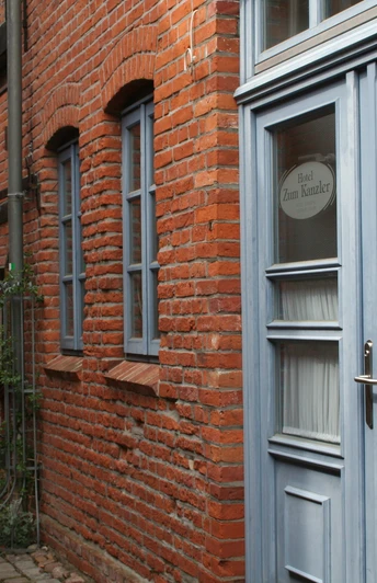 Historische Backsteinfassade eines Hotels mit blauen Fenstern und Türen in einer schmalen Gasse.