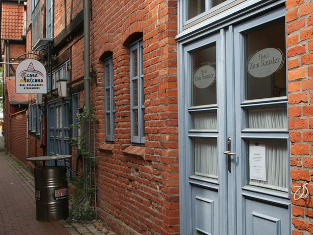 Historic brick façade of a hotel with blue windows and doors in a narrow alley.