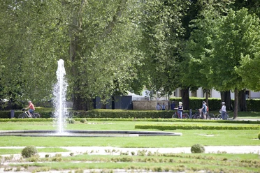 Radfahrer genießen den großzügigen Schloss- und Auenpark mit sprudelndem Brunnen und viel Grün.