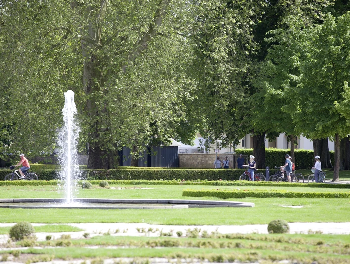 Radfahrer genießen den großzügigen Schloss- und Auenpark mit sprudelndem Brunnen und viel Grün.
