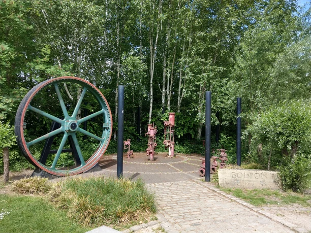 Partnerschaftsgarten der Stadt Bolten Historischer Industriestandort im Grünen: altes Rad und Ventile umgeben von Bäumen in Bolten.