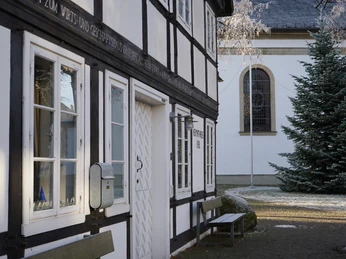 Heimathaus Fachwerkhaus neben einer Kirche im Winter, mit dekorativem Weihnachtsbaum und leichtem Rauhreif.