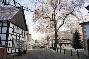 Malerische Fachwerkhäuser mit verschneiten Bäumen säumen eine ruhige, charmante Straße im Winter.
