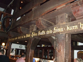 Holzvertäfelte Bar mit traditionellem Schriftzug und historischen Balken; darunter gemütlicher Tresen.