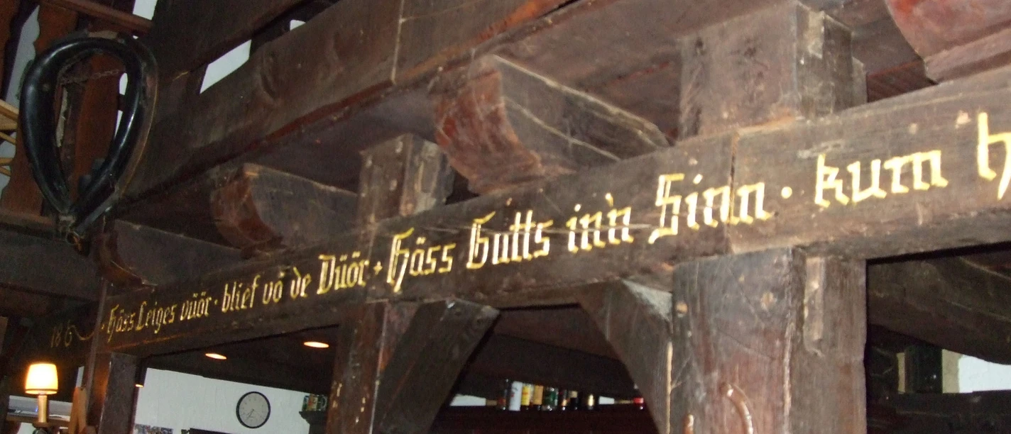 Tenne.jpg Holzvertäfelte Bar mit traditionellem Schriftzug und historischen Balken; darunter gemütlicher Tresen.