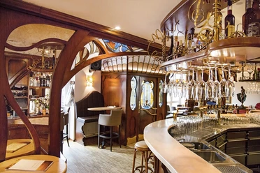 Lamäng_2.jpg Gemütliche Bar im Jugendstil, geschwungene Holzelemente, stilvolle Hängelampen, einladende Atmosphäre.