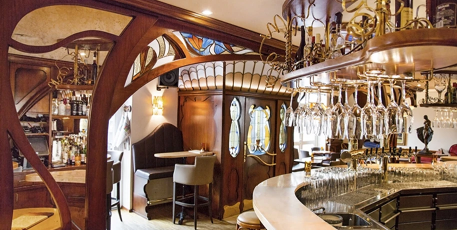 Lamäng_2.jpg Gemütliche Bar im Jugendstil, geschwungene Holzelemente, stilvolle Hängelampen, einladende Atmosphäre.