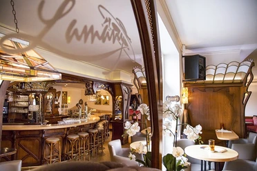 Gemütliches Café mit Holzeinrichtung und Barhockern, warm beleuchtet, mit Orchideen am Tisch.
