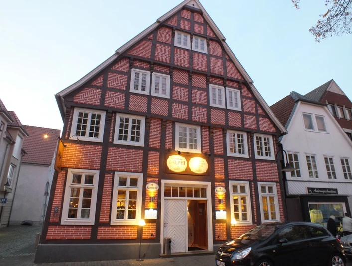 Fachwerkhaus bei Dämmerung, rot-weiße Ziegel, weiße Fensterrahmen, beleuchtete Gasthausreklame.