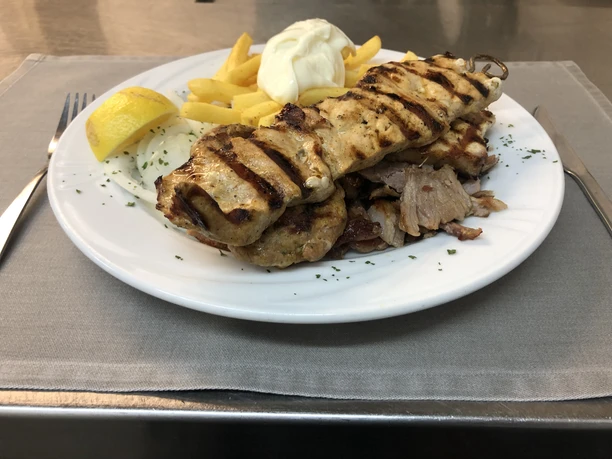 Ein köstlicher Teller mit gegrilltem Fleischspieß, Pommes, Zitronenviertel und Sahnehäubchen.