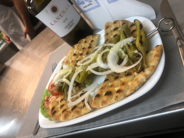 Gegrilltes Fladenbrot mit Zwiebeln und Peperoni serviert auf weißem Teller mit griechischem Wein.