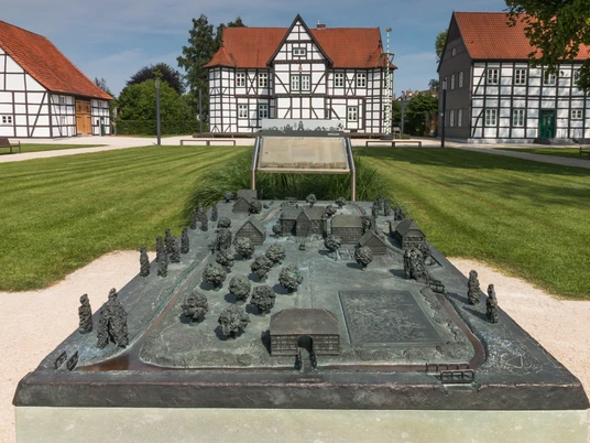 Ein detailliertes Bronzemodell des Jagdschlosses in Hövelhof mit Fachwerkhäusern im Hintergrund.