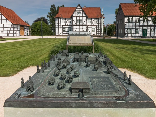 Jagdschloss Hövelhof Ein detailliertes Bronzemodell des Jagdschlosses in Hövelhof mit Fachwerkhäusern im Hintergrund.