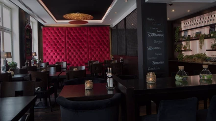 Gemütliches Restaurant mit modernen, dunklen Holzmöbeln, roter samtverzierter Wand und Kerzenlicht.