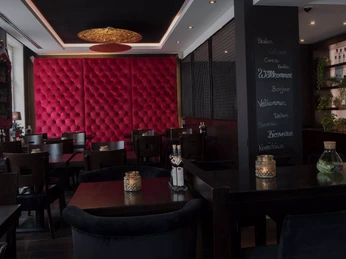 Königs_1.png Gemütliches Restaurant mit modernen, dunklen Holzmöbeln, roter samtverzierter Wand und Kerzenlicht.