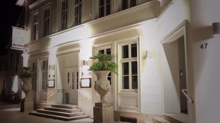 Elegante Fassade eines historischen Gebäudes bei Nacht mit warm beleuchteten Fenstern und Palmen.