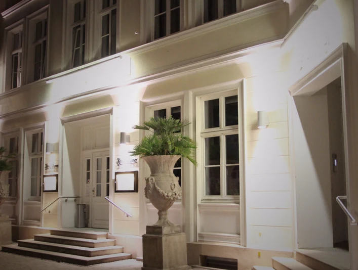 Elegante Fassade eines historischen Gebäudes bei Nacht mit warm beleuchteten Fenstern und Palmen.