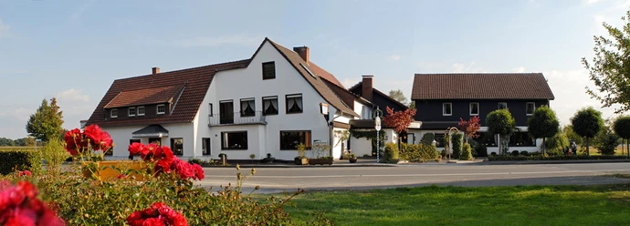 Großer, traditioneller Gasthof mit weißer Fassade und rotem Ziegeldach, umgeben von blühenden Rosen.