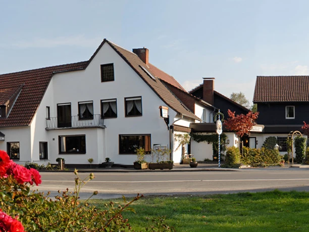 Großer, traditioneller Gasthof mit weißer Fassade und rotem Ziegeldach, umgeben von blühenden Rosen.