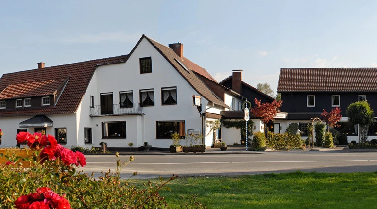 Großer, traditioneller Gasthof mit weißer Fassade und rotem Ziegeldach, umgeben von blühenden Rosen.