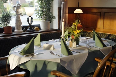 Ein elegant gedeckter Tisch in einem gemütlichen Restaurant, mit grünen Servietten und Blumen.