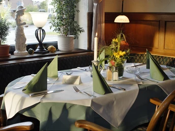 Ein elegant gedeckter Tisch in einem gemütlichen Restaurant, mit grünen Servietten und Blumen.