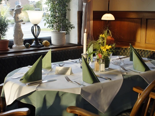Pöppelbaum_2.jpg Ein elegant gedeckter Tisch in einem gemütlichen Restaurant, mit grünen Servietten und Blumen.
