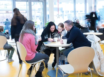Menschen sitzen in einem modernen Café an einem Tisch, genießen warme Getränke und unterhalten sich.