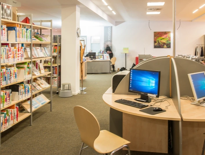 Bibliothek mit Bücherregalen, Computertischen und Lesestühlen in einem modernen und einladenden Raum.