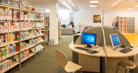 Bibliothek_Rheda_Internet.jpg Bibliothek mit Bücherregalen, Computertischen und Lesestühlen in einem modernen und einladenden Raum.