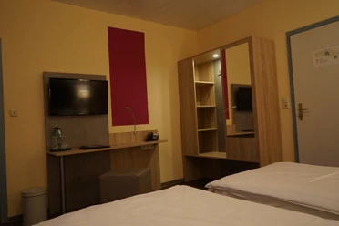 Doppelzimmer mit modernen Holzmöbeln, Flachbildfernseher, Schreibtisch und warmen Wandfarben.