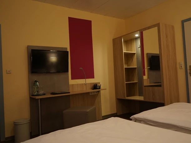 Zimmer Bonneberger Hof Doppelzimmer mit modernen Holzmöbeln, Flachbildfernseher, Schreibtisch und warmen Wandfarben.