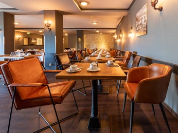 Innenansicht eines Restaurants mit modernen, braunen Ledersesseln und Tischen, warmes Ambiente.