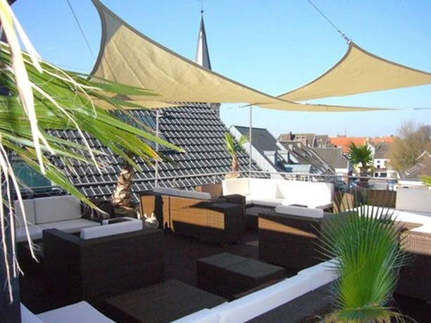 Königs_Rheda_1.jpg Dachterrasse mit modernen Rattanmöbeln, Sonnensegeln und Blick auf Kirchturm und umliegende Dächer.