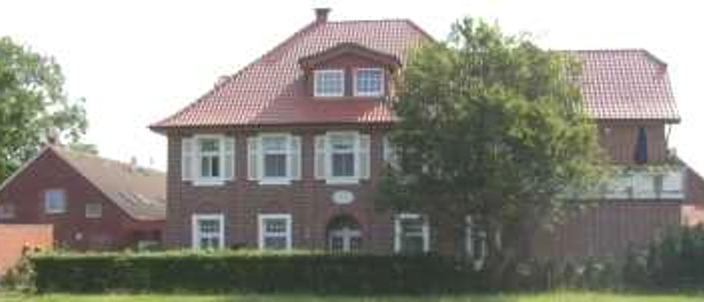 Biermann_1.jpg Backsteinhaus mit rotem Dach in ländlicher Umgebung, üppiges Grün und blauer Himmel im Hintergrund.