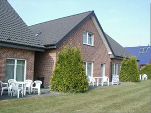 City-Appartements_1.jpg Reihenhaus mit Ziegelsteinfassade und Gartenmöbeln im Vorgarten, sonniger Tag.