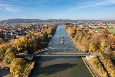 Panoramablick auf den Mittellandkanal bei Bad Essen Brücke über einen herbstlichen Fluss mit Frachtschiff, umgeben von buntem Laub.