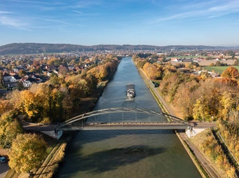 Panoramablick auf den Mittellandkanal bei Bad Essen Brücke über einen herbstlichen Fluss mit Frachtschiff, umgeben von buntem Laub.Bridge over an autumnal river with a cargo ship, surrounded by colorful foliage.Bro over en efterårsagtig flod med et fragtskib, omgivet af farverigt løv.Brug over een herfstige rivier met een vrachtschip, omringd door kleurrijk gebladerte.