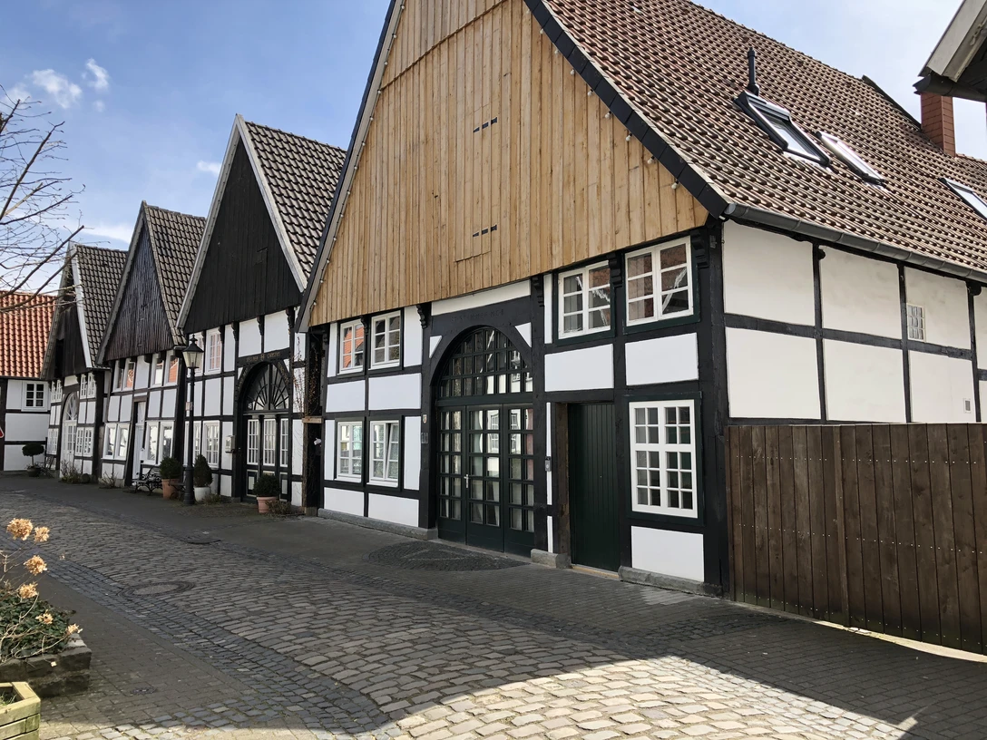 Fachwerkhäuser in einer ruhigen Kopfsteinpflastergasse mit blauen Himmel und vereinzelten Wolken.