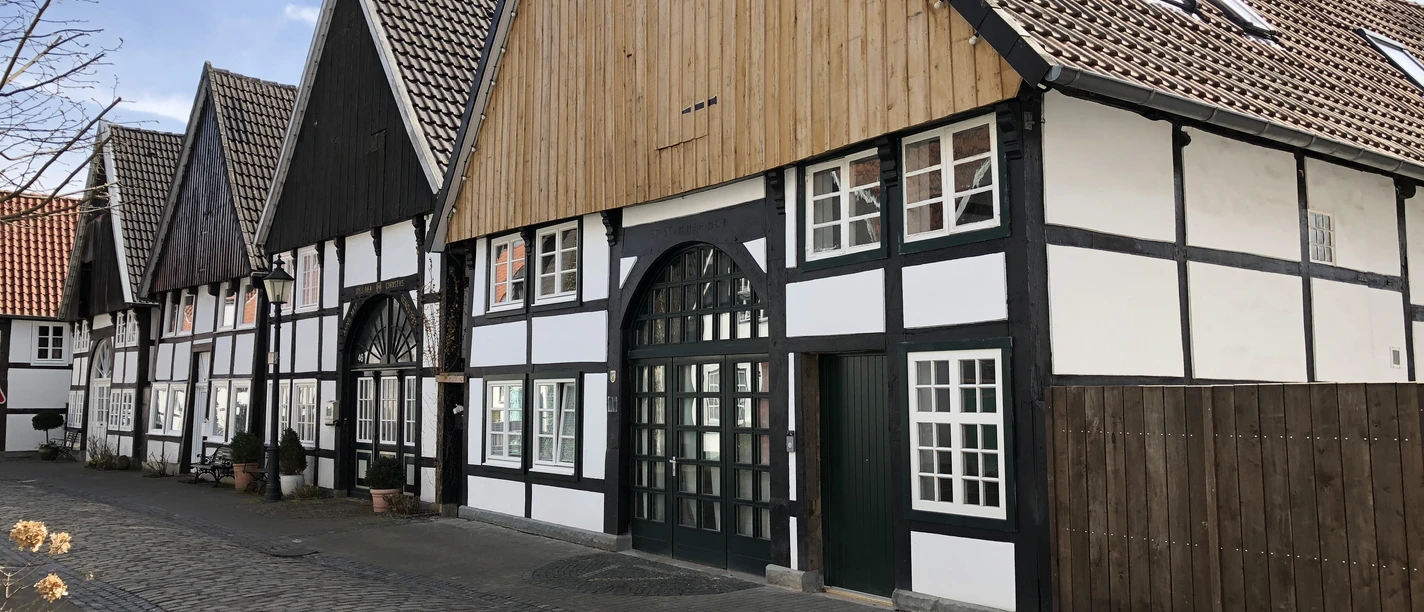 Fachwerkhäuser in einer ruhigen Kopfsteinpflastergasse mit blauen Himmel und vereinzelten Wolken.
