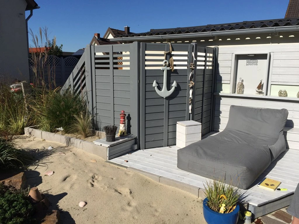 Ein gemütlicher Terrassenbereich mit Liegestuhl, umgeben von Sand und maritimen Dekorationen.