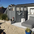 Ein gemütlicher Terrassenbereich mit Liegestuhl, umgeben von Sand und maritimen Dekorationen.