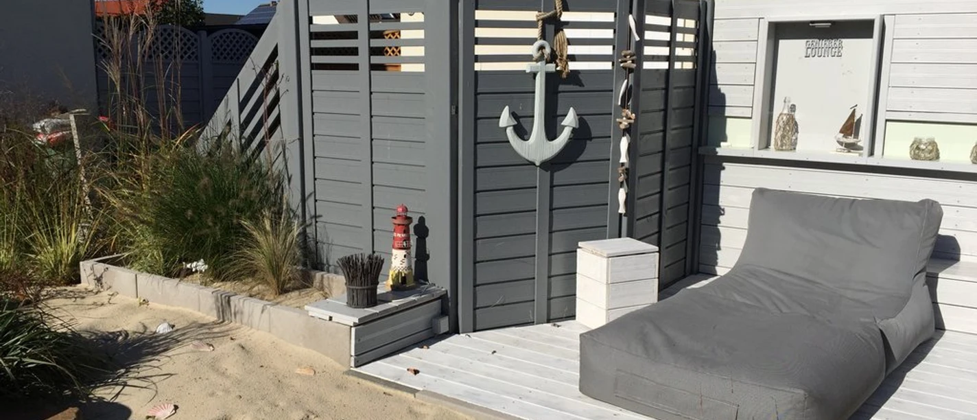 Ein gemütlicher Terrassenbereich mit Liegestuhl, umgeben von Sand und maritimen Dekorationen.