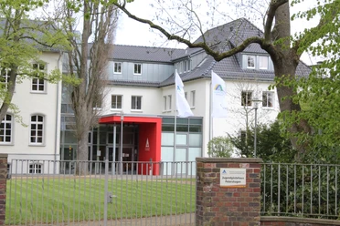 Jugendherberge Petershagen Jugendherberge Petershagen mit modernem Eingang, zwei Flaggen und grünem Rasen, umgeben von Bäumen.