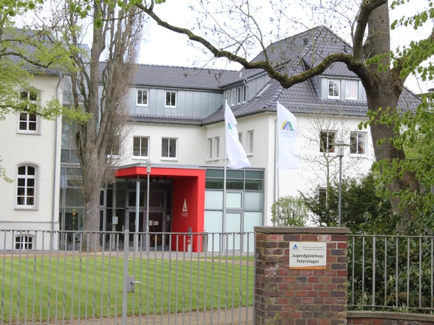 Jugendherberge Petershagen Jugendherberge Petershagen mit modernem Eingang, zwei Flaggen und grünem Rasen, umgeben von Bäumen.
