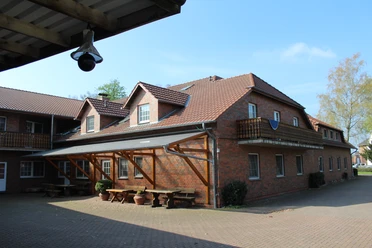 Ferienhof Meyer Ein Backsteingebäude mit Flachdach und Balkonen vor blauem Himmel und bepflastertem Hofweg.