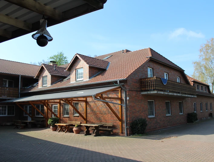 Ferienhof Meyer Ein Backsteingebäude mit Flachdach und Balkonen vor blauem Himmel und bepflastertem Hofweg.