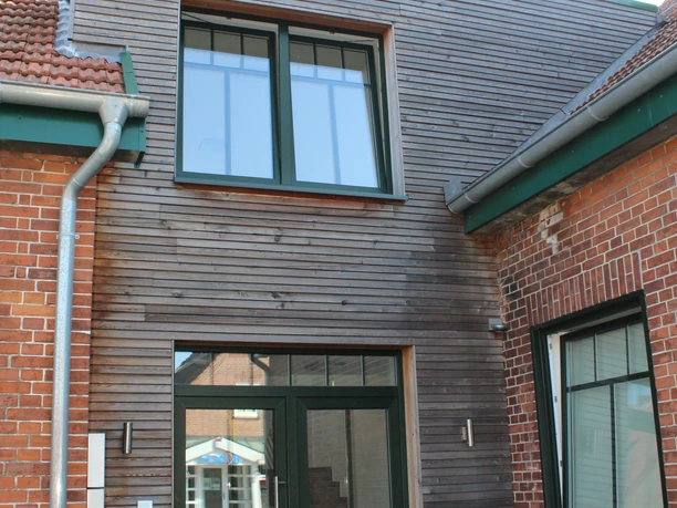 Gästezimmer Bär Backsteinbau mit modernem Holzanbau, zwei großen Fenstern und Türen, im Innenhof mit Pflanzen.