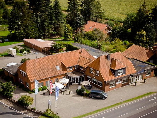 Neuloher Hof Luftaufnahme eines Backsteingebäudes mit Ziegeldach, flankiert von Bäumen und landwirtschaftlichen Feldern.