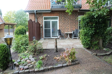 FeWo "An der Hache" Ziegelhaus mit heller Terrasse, umgeben von Pflanzen und Gartenmöbeln, bei sonnigem Wetter.